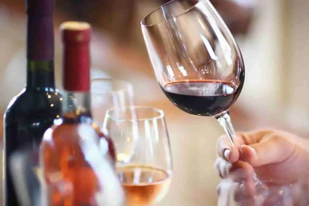 Main tenant un verre de vin rouge incliné devant plusieurs bouteilles, image qui évoque la richesse aromatique du vin de noix