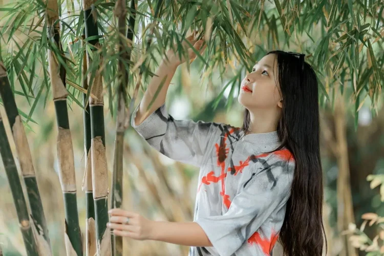 Personne en tenue traditionnelle touchant feuilles de bambou au milieu de tiges vertes illustrant idée de multiplier les bambous dans un cadre naturel.