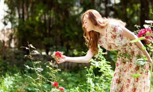 Personne aux cheveux roux tenant une rose rouge reflétant la richesse sensorielle d’un jardin olfactif.