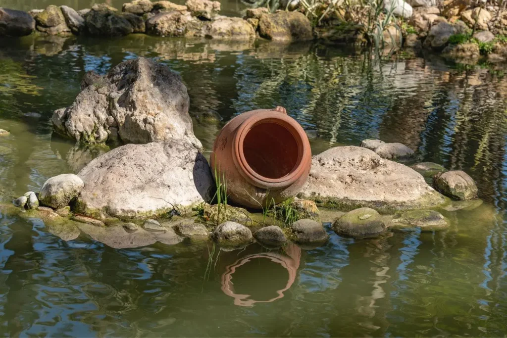 Bassin naturel entouré de pierres avec jarre en terre cuite, image qui illustre l’entretien d’un bassin de jardin pour préserver son charme.