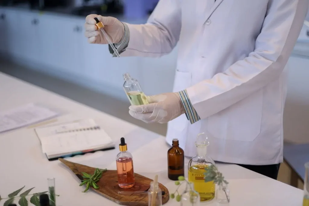 Scientifique en blouse blanche manipule flacon jaune, image illustrant la préparation d’une huile infusée aux herbes aromatiques.