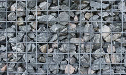 Structure métallique remplie de pierres grises et brunes, image illustrant un mur en gabion utilisé pour stabiliser et décorer un espace extérieur.