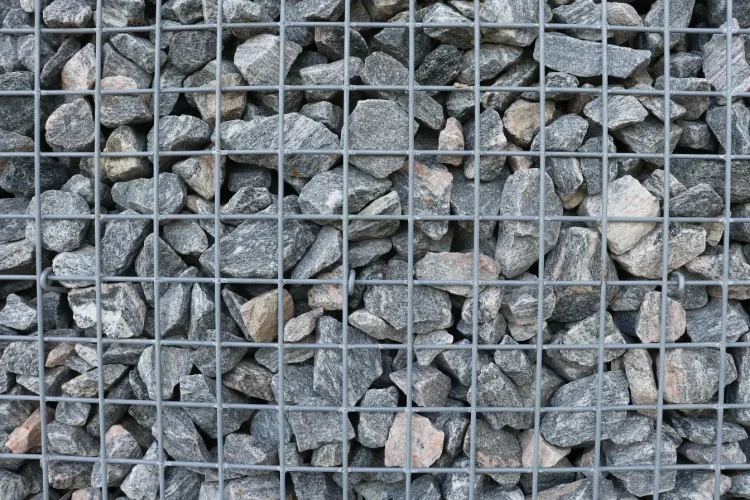 Structure métallique remplie de pierres grises et brunes, image illustrant un mur en gabion utilisé pour stabiliser et décorer un espace extérieur.