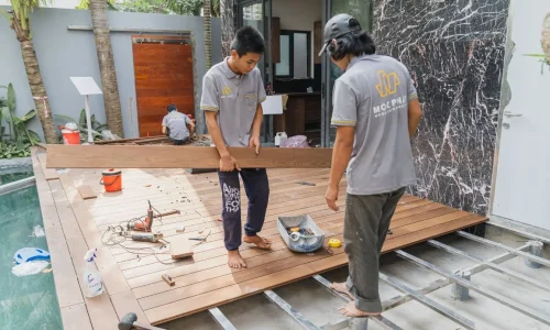 Trois personnes installant des lames de bois près d’une piscine, image qui illustre la pose d’une terrasse en bois composite réalisée soi-même.