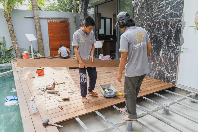 Trois personnes installant des lames de bois près d’une piscine, image qui illustre la pose d’une terrasse en bois composite réalisée soi-même.