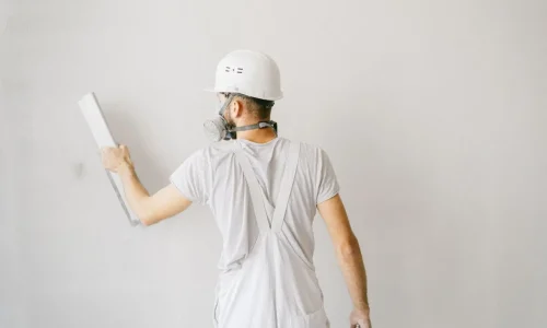 Personne en combinaison blanche et casque appliquant un outil sur un mur, image qui illustre la réalisation d’un enduit à la chaux naturelle.