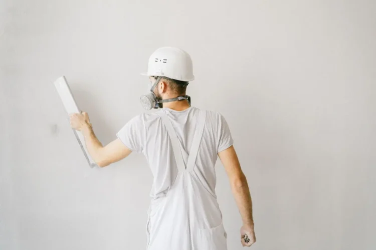 Personne en combinaison blanche et casque appliquant un outil sur un mur, image qui illustre la réalisation d’un enduit à la chaux naturelle.