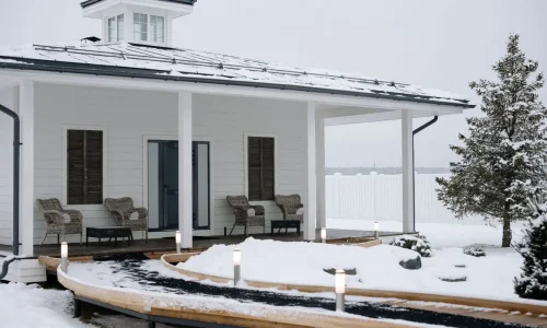 Véranda accueillante en hiver, décorée de fauteuils confortables et lumières douces, offrant un espace chaleureux malgré la neige environnante.