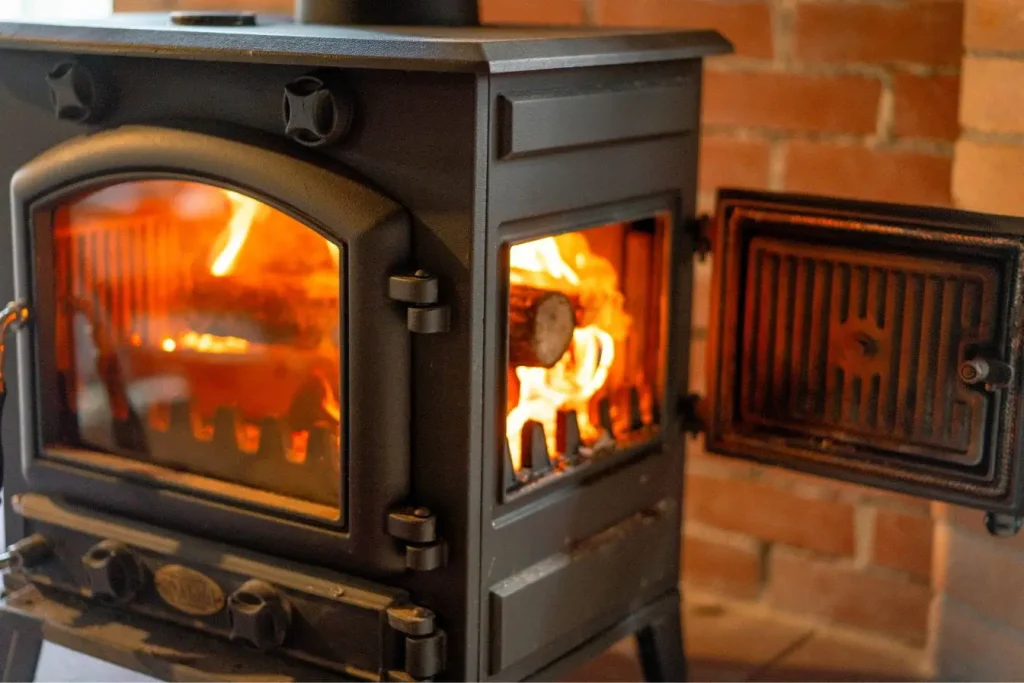 Poêle en fonte noir avec flammes visibles derrière la vitre, image qui illustre la chaleur et le confort apportés par l’installation d’un poêle à bois.