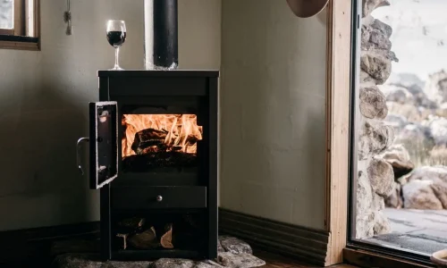 Poêle noir avec flammes visibles et verre de vin posé dessus, image qui illustre l’ambiance chaleureuse et l’idée d’installer un poêle à bois chez soi.