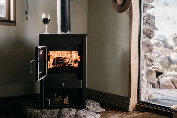 Poêle noir avec flammes visibles et verre de vin posé dessus, image qui illustre l’ambiance chaleureuse et l’idée d’installer un poêle à bois chez soi.