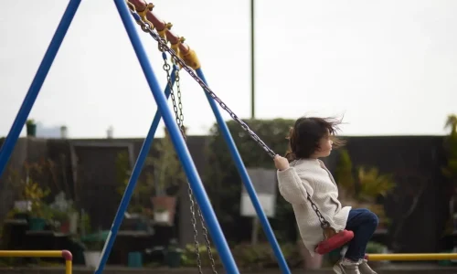 Enfant assis sur une balançoire rouge suspendue à une structure bleue, image qui illustre le plaisir d’installer une balançoire de jardin.