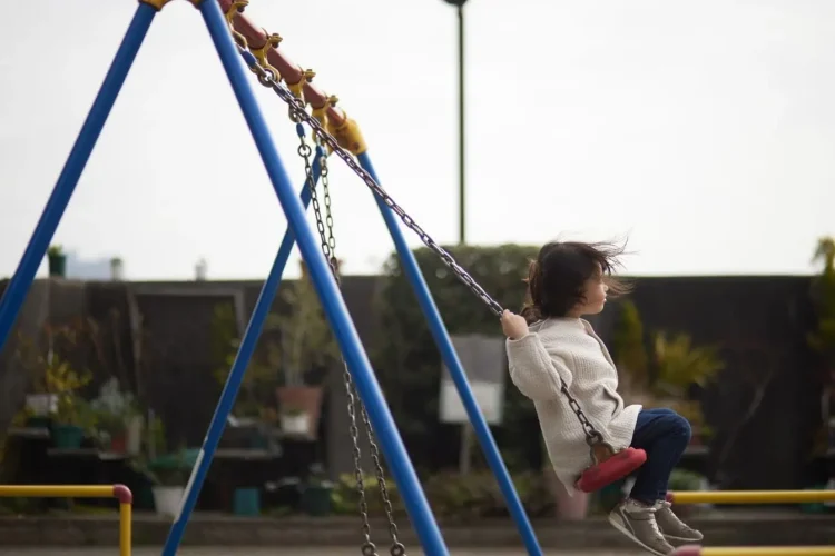 Enfant assis sur une balançoire rouge suspendue à une structure bleue, image qui illustre le plaisir d’installer une balançoire de jardin.