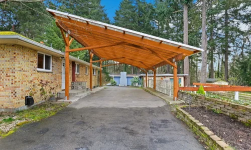 Maison en briques avec carport en bois robuste, image qui illustre la possibilité d’installer soi-même une structure pratique et esthétique.