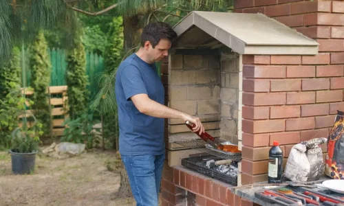 Personne en t-shirt bleu cuisinant sur barbecue en briques dans un jardin verdoyant, reflet d’un coin barbecue convivial.