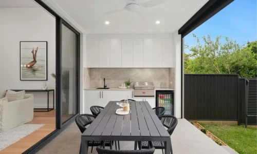 Terrasse moderne avec grande table grise et chaises noires, image qui illustre un coin repas convivial ouvert sur le salon et le jardin.