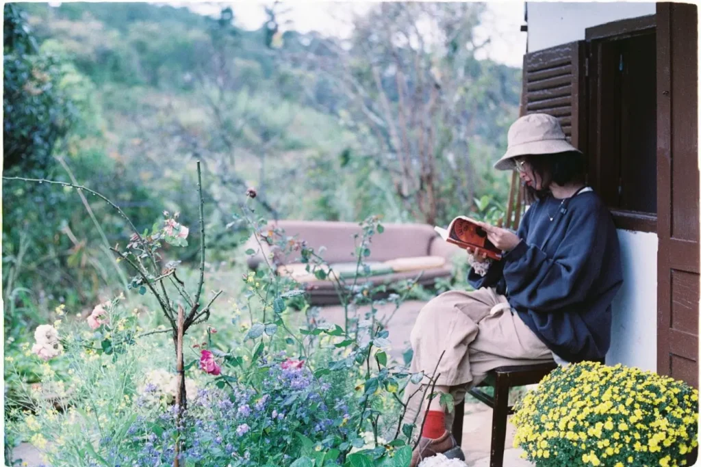 Personne assise sur chaise en bois lisant un livre, entourée de fleurs colorées et verdure, image qui illustre un coin lecture paisible au jardin.