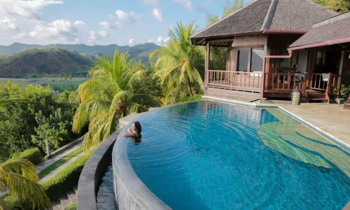 Piscine à débordement entourée de palmiers et villa bois, image qui illustre l’importance d’hiverner correctement une piscine hors-sol.