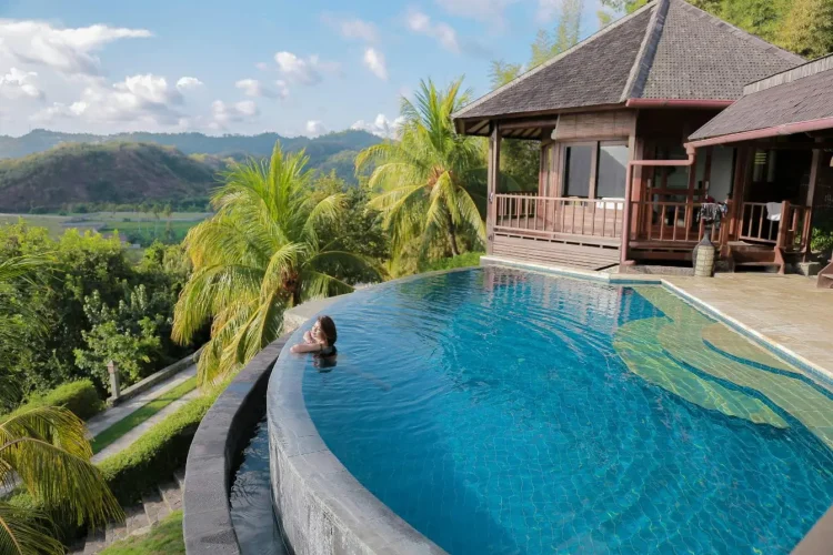Piscine à débordement entourée de palmiers et villa bois, image qui illustre l’importance d’hiverner correctement une piscine hors-sol.