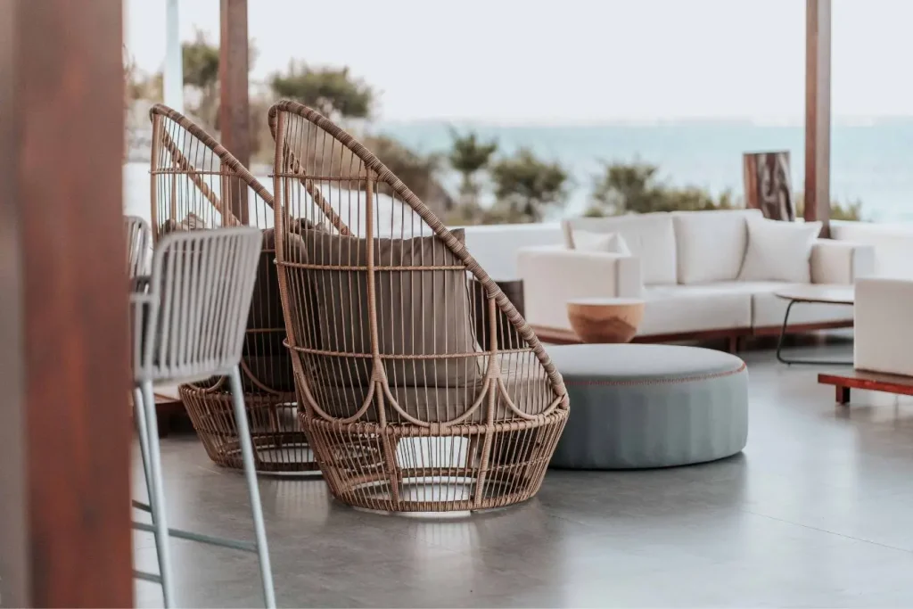 Terrasse extérieure moderne avec sol bois, fauteuils en rotin et canapé blanc, mettant en valeur revêtement élégant face à vue océan.