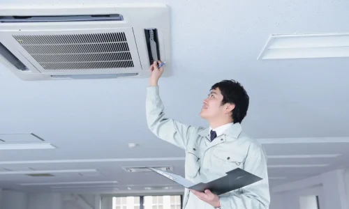 Technicien en uniforme gris vérifiant climatiseur au plafond, reflet des pratiques d’entretien d’un climatiseur réversible.