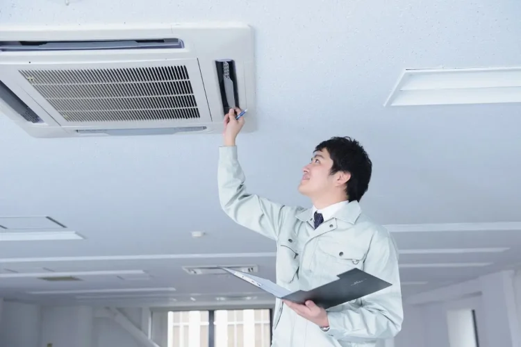 Technicien en uniforme gris vérifiant climatiseur au plafond, reflet des pratiques d’entretien d’un climatiseur réversible.