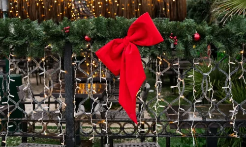 Guirlande de sapin ornée de baies rouges et grand nœud rouge, image qui illustre les décorations de Noël pour l’extérieur.