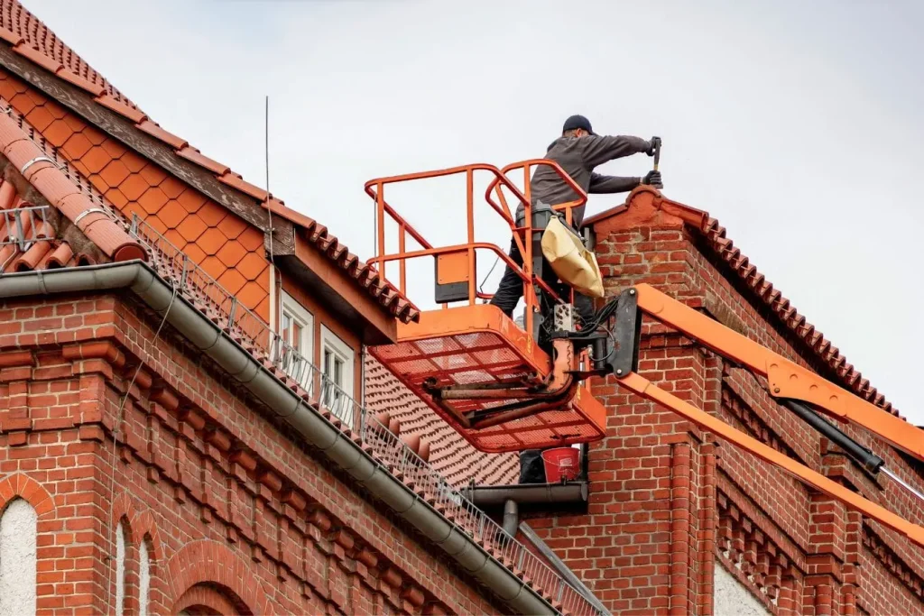 Ouvrier sur nacelle effectuant maintenance près de cheminée, reflet de l’entretien des gouttières de toiture pour prévenir infiltrations.