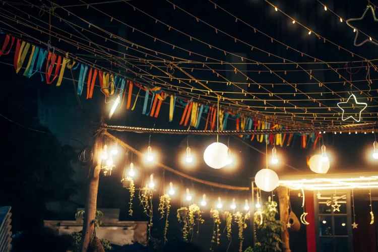 Guirlandes lumineuses suspendues avec étoiles et lune, image qui illustre une guirlande solaire de jardin.