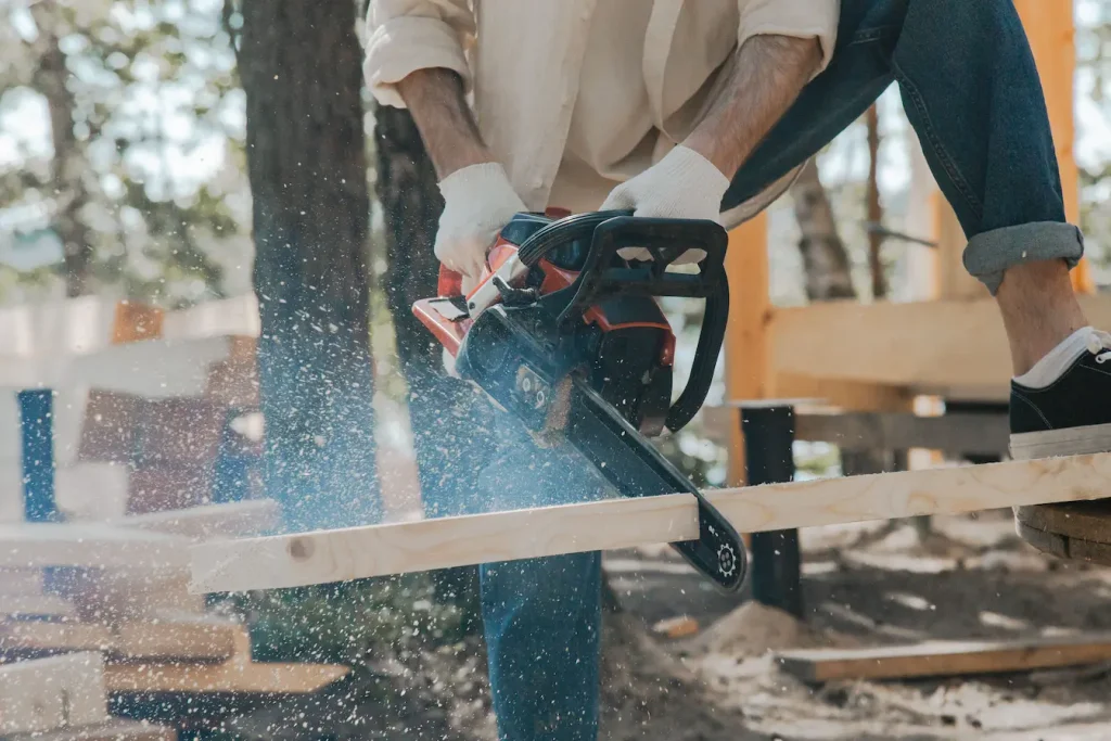 Personne en gants blancs utilisant tronçonneuse rouge et noire sur planche bois, reflet du choix entre tronçonneuse thermique ou électrique.