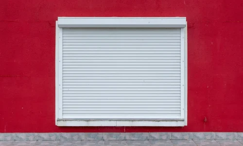 Volet roulant blanc fermé sur mur rouge vif, image qui illustre l’entretien d’un volet roulant électrique et la durabilité du mécanisme.