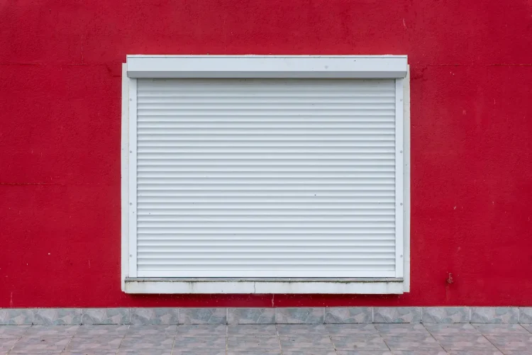 Volet roulant blanc fermé sur mur rouge vif, image qui illustre l’entretien d’un volet roulant électrique et la durabilité du mécanisme.