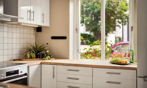Cuisine lumineuse avec plan de travail en bois clair sous une grande fenêtre, illustrant un matériau chaleureux et apprécié pour aménager une cuisine conviviale