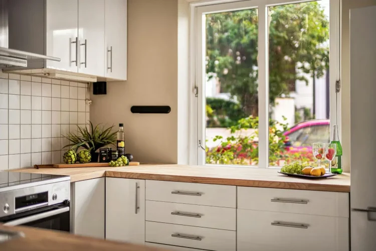 Cuisine lumineuse avec plan de travail en bois clair sous une grande fenêtre, illustrant un matériau chaleureux et apprécié pour aménager une cuisine conviviale