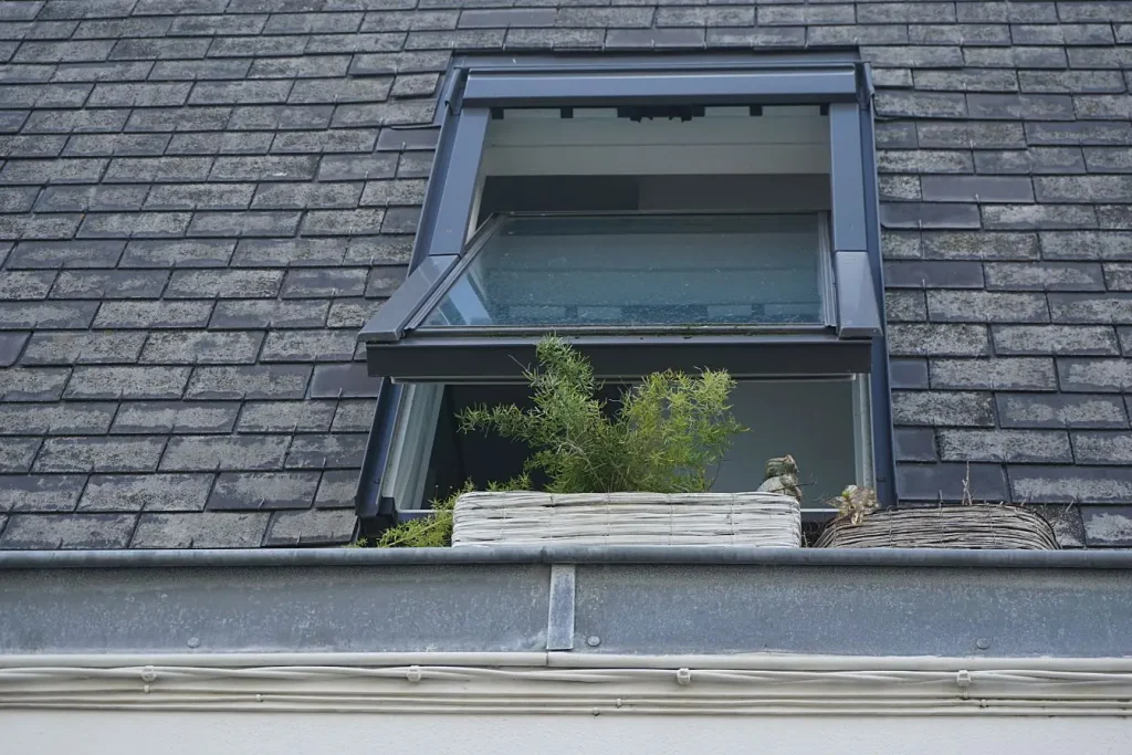 Fenêtre de toit ouverte sur une toiture en ardoise, une image idéale pour illustrer la différence entre un Velux et une fenêtre de toit classique