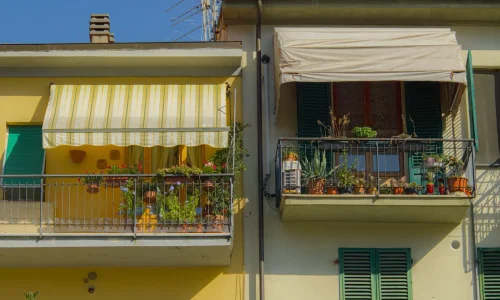 Deux balcons voisins ornés de plantes, l’un avec auvent rayé jaune et blanc, symbole de l’installation d’un auvent au-dessus d’une terrasse.