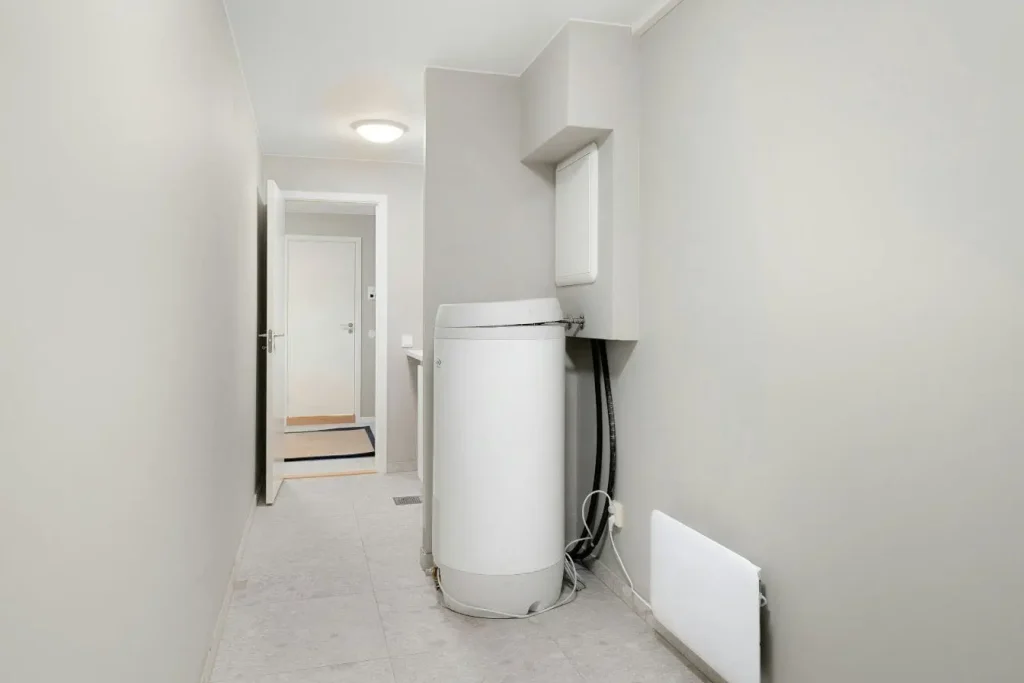 Chauffe-eau cylindrique installé dans pièce étroite avec tuyaux visibles, symbole des gestes pour détartrer soi-même.