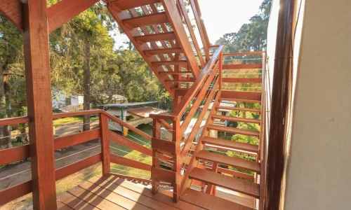Escalier en bois rougeâtre avec câbles métalliques, symbole des projets de rénovation extérieure.