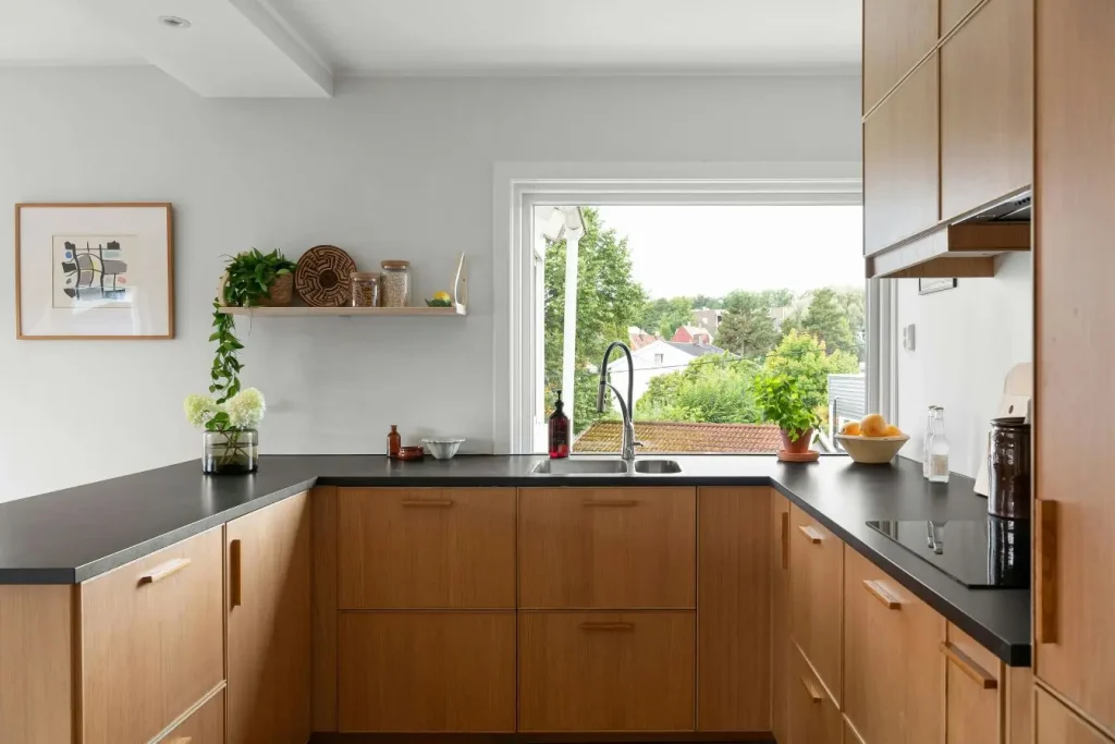 Cuisine moderne avec meubles en bois clair et plan de travail sombre sous une grande fenêtre, illustrant le choix d’un matériau durable et élégant pour la cuisine